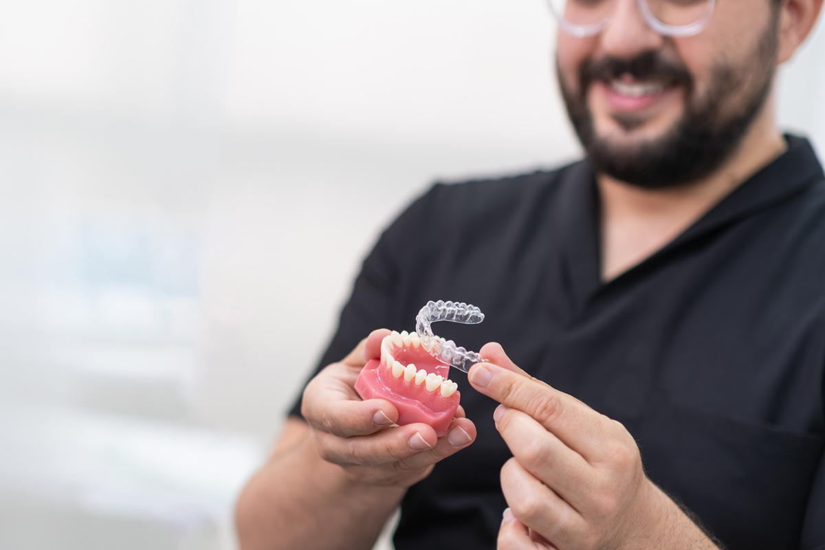 Bearded orthodontist putting transparent aligners on artificial lower jaw in stomatology clinic