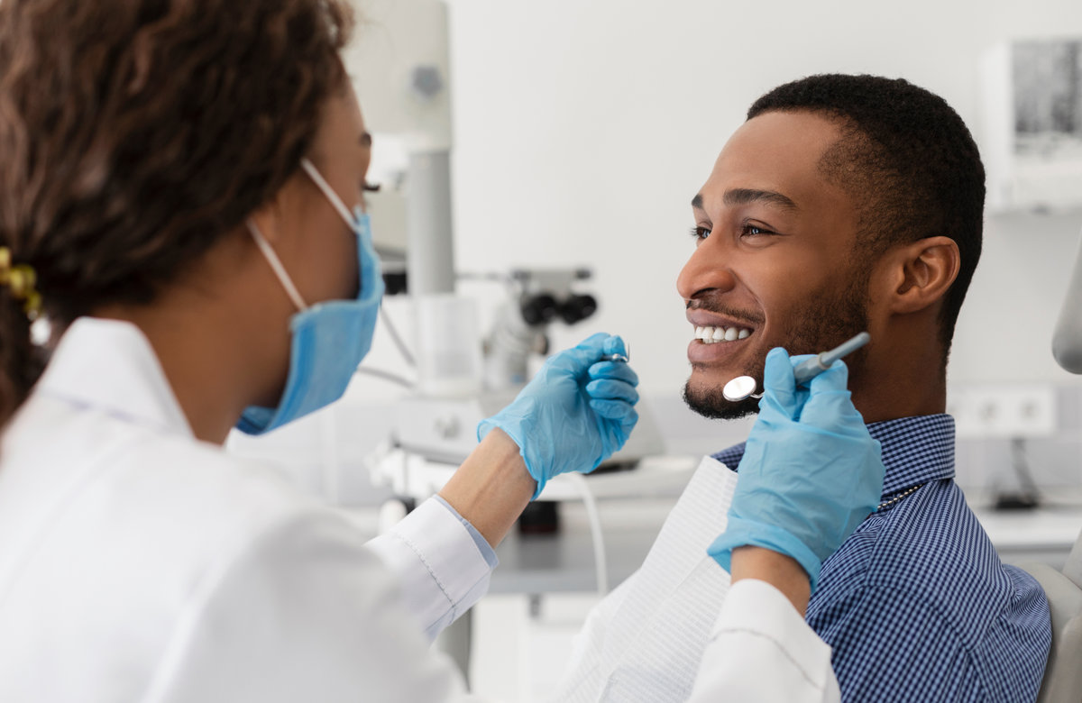 Young african guy smiling to his female dentist while having treatment at modern clinic