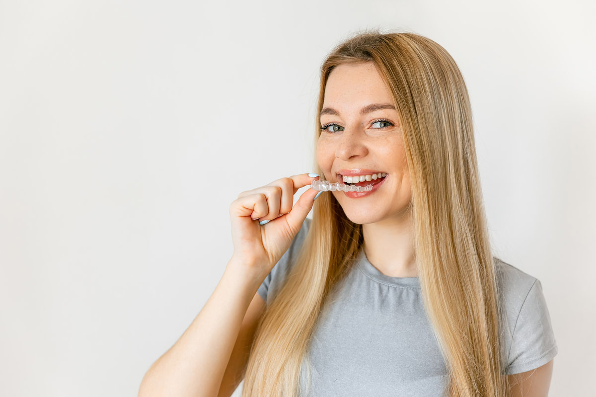 Dental care. Smiling woman with healthy teeth using removable clear braces aligner, orthodontic silicone trainer.